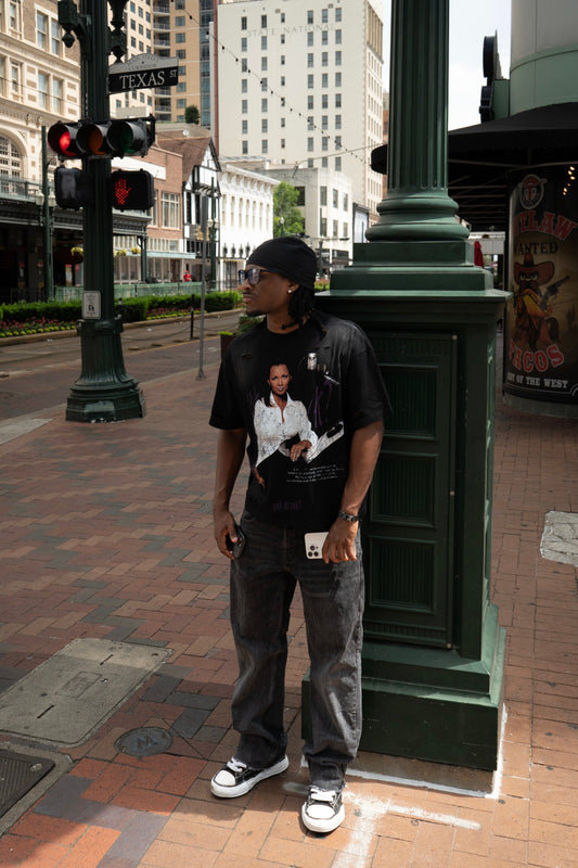 Man standing on a city street corner wearing a black t-shirt with a graphic design.