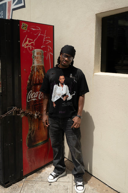 Person wearing a black t-shirt with a graphic design, standing next to a Coca-Cola vending machine.